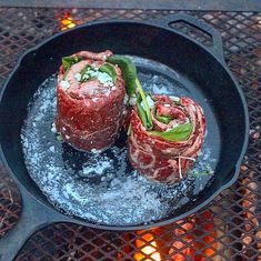 two pieces of meat are cooking in a skillet on the fire pit with tongs