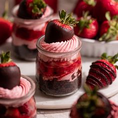 several desserts in small glass jars with strawberries on the top and one chocolate covered strawberry