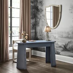 a desk with a mirror and lamp in front of a wallpapered room that has trees on it