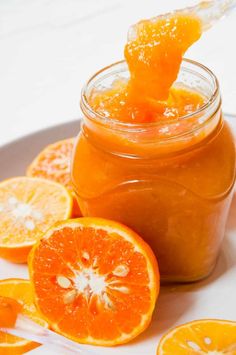 an orange jam in a glass jar on a plate with sliced oranges around it