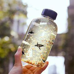 a hand holding a bottle filled with birds flying through the air and food in it