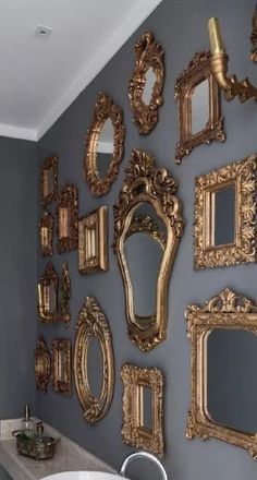 there are many mirrors on the wall in this bathroom, one is gold and the other is silver