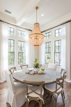 the dining room table is set with white chairs and a chandelier above it