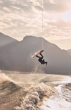 a person on a surfboard in the air above the water with mountains in the background