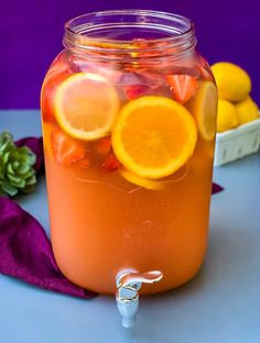 a mason jar filled with oranges and lemon slices on top of a purple cloth