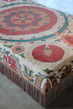 an ornately decorated ottoman with fringes on the top and bottom, sitting in a room