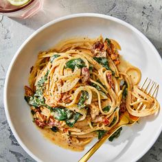 a white bowl filled with pasta and spinach on top of a marble countertop