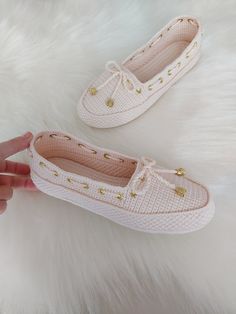 a pair of white shoes with gold studdings on the side and one being held up by someone's hand