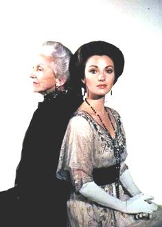 two women are standing next to each other in formal dress and gloves, one is wearing an evening gown