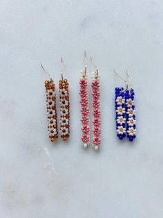 three pairs of beaded earrings sitting on top of a white surface, each with different colored beads