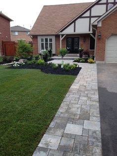 a brick walkway leading to a house with grass and flowers in the front yard area