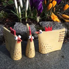 two ceramic chickens with red heads are standing next to each other on the ground in front of flowers