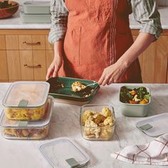 a woman in an apron preparing food on a kitchen counter with plastic containers and utensils