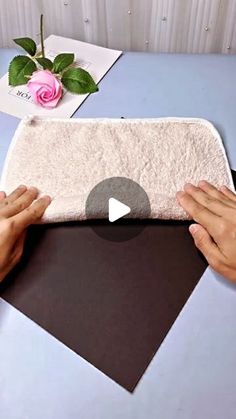 two hands are holding a towel on top of a table next to a pink rose