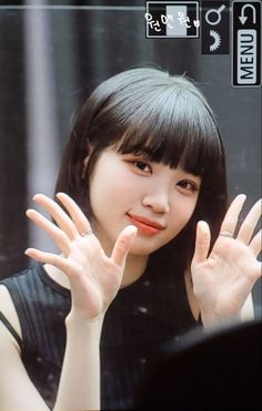 a woman with black hair and bangs holding her hands up in front of her face