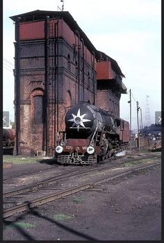 an old train sits on the tracks in front of a building with a star painted on it