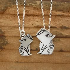 two silver necklaces sitting on top of a piece of wood with one holding the other's head