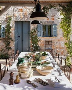 an outdoor dining table with plates and utensils laid out on it in front of a stone building