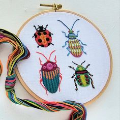 three different colored bugs on a white wall hanging in front of a thread spool