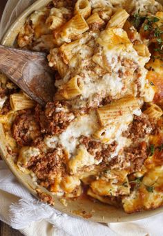 a bowl full of pasta and meat with a wooden serving spoon in it on a white cloth