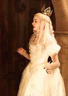 a woman in a white dress with a crown on her head standing next to a door