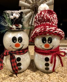 two snowmen with hats and scarfs on top of a counter next to each other