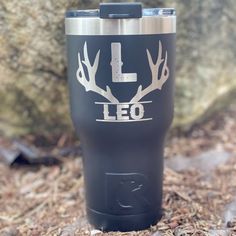 a black tumbler cup with white deer antlers and the word leo on it