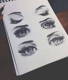 an open notebook with drawings of eyes and lashes on it, next to a pen