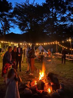 people gathered around a campfire at night with lights strung over the campsite and trees in the background