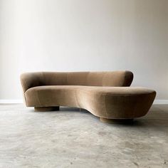 a curved couch sitting on top of a cement floor next to a white wall in an empty room