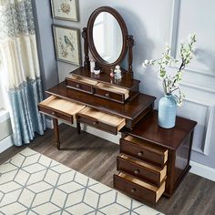 a vanity with drawers and a mirror on the wall next to a vase filled with flowers