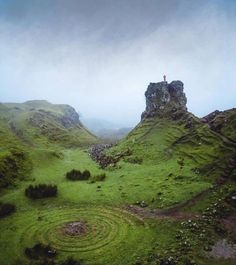 a person standing on top of a green hill with a spiral in the grass below