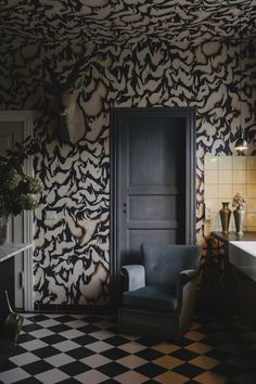 a black and white checkered floor with a chair in front of a wallpapered room