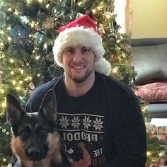 a man wearing a santa hat sitting next to a dog in front of a christmas tree