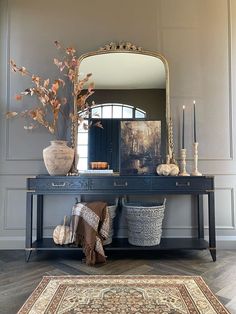 a table with a mirror, vases and other items on it in front of a rug