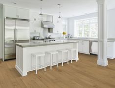 a large kitchen with white cabinets and counter tops, along with four stools in front of the island