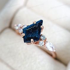 a blue diamond ring sitting on top of a white cushion