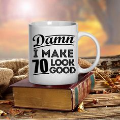 a white coffee mug with the words damn i make 75 look good on top of a stack of books