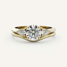 a yellow and white gold engagement ring with two diamonds on the side, in front of a plain background