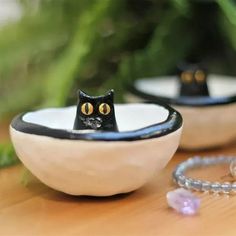 a black cat sitting in a white bowl on top of a table next to a key chain