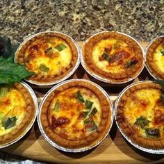 there are many small pies on the wooden platter with green leafy garnishes