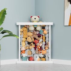 a bunch of stuffed animals in a cage on top of a shelf next to a potted plant