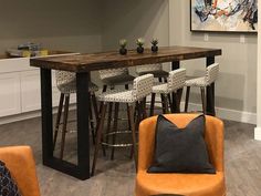 a living room filled with furniture next to a kitchen table and bar stools in front of a painting