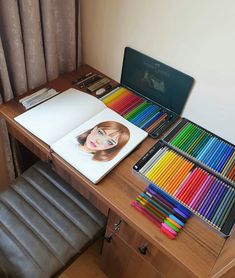 an open book sitting on top of a wooden desk next to a bunch of colored pencils