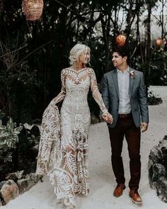 a man and woman holding hands walking down a path in front of some trees with lights hanging from them