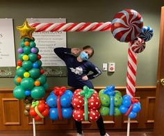 a man standing in front of a christmas tree made out of balloons and candy canes