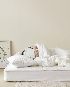 a person laying in bed under a white blanket and reading a book with their head on the pillow