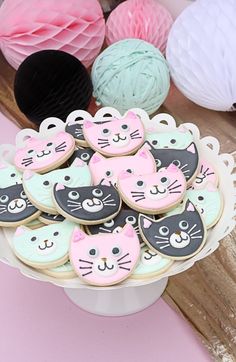 decorated cookies in the shape of cats and kittens on a cake plate with balls of yarn behind them