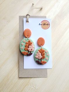 a pair of earrings with flowers on them sitting on top of a wooden table next to a card