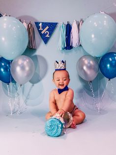 a baby is sitting on the floor with balloons and streamers around him, wearing a blue diaper